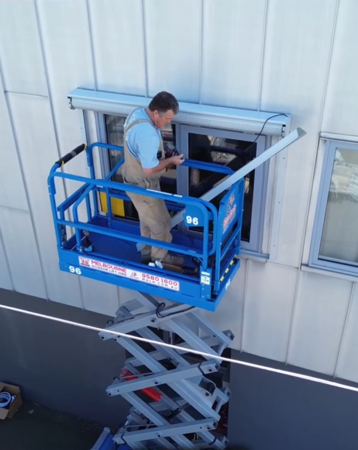 Chris on a blue EWP scissor lift installing a shutter on a commercial building